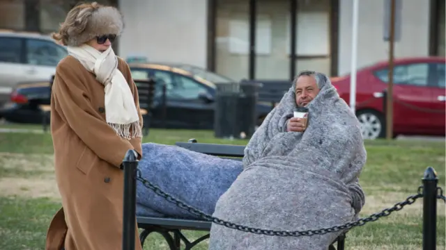 واشنگٹن ڈی سی کے میکفرسن سکوائر میں گرم لباس میں ملبوس ایک عورت ایک بے گھر شخص کے پاس سے گزر رہی ہے