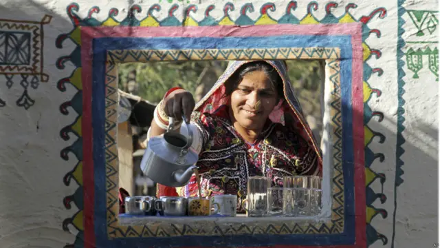 कच्छ में स्थित हुडको गांव में एक महिला अपने घर की खिड़की से ग्राहकों को चाय दे रही है. नए साल के मौके पर यहां घरों को आकर्षक ढंग से सजाया गया है.