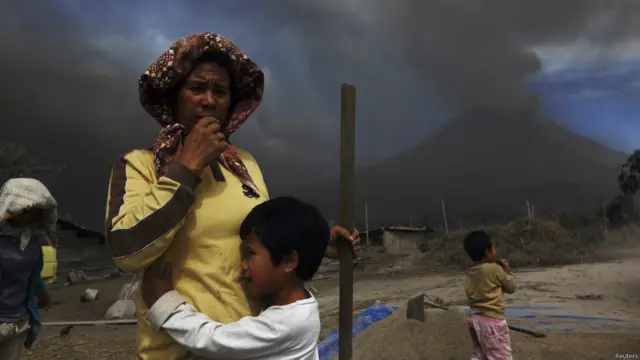 Seorang anak memeluk ibunya di samping tumpukan benih padi