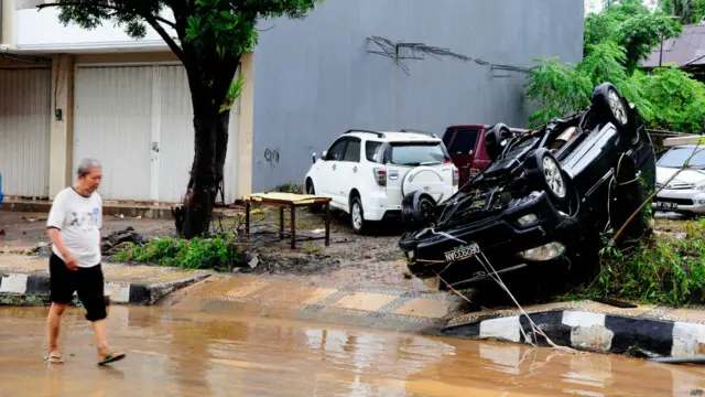 Seorang warga melewati mobil yang terbalik akibat banjir bandang