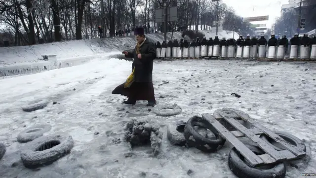 यूक्रेन में पुलिस और सरकार विरोधी प्रदर्शनकारियों के बीच एक पादरी घटनास्थल पर जाते हुए. संसद ने वहां विरोध प्रदर्शनों के खिलाफ पांबदी लगाने वाले कानून को रद्द किया है.