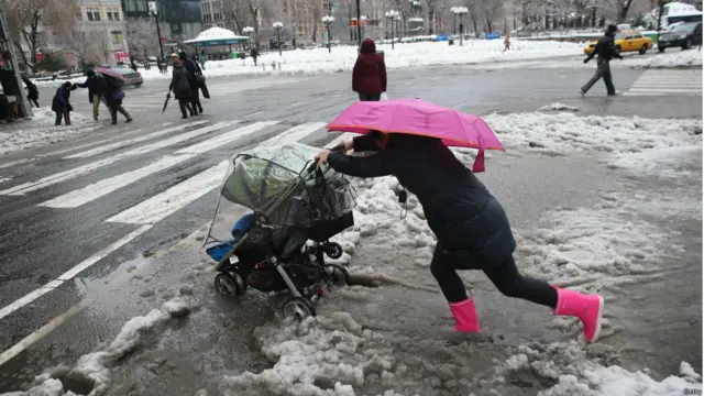Seorang pengasuh anak berusaha mendorong kereta dorong melewati persimpangan jalan
