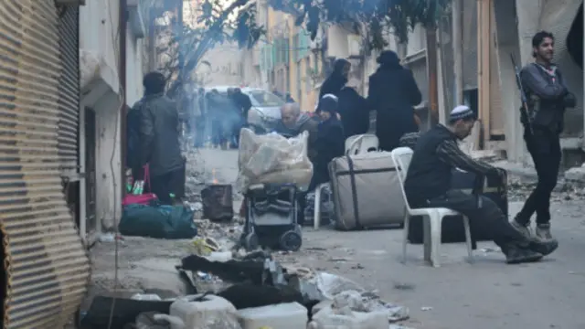 شام کے تیسرے بڑے شہر حمص میں پھنسے ہوئے عام شہری اپنا ساز وسامان لیے باغیوں کے زیر تسلط علاقے کی ایک گلی میں بیٹھے ہوئے ہیں