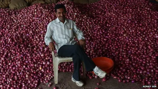 प्याज के ढेर के सामने बैठा थोक विक्रेता