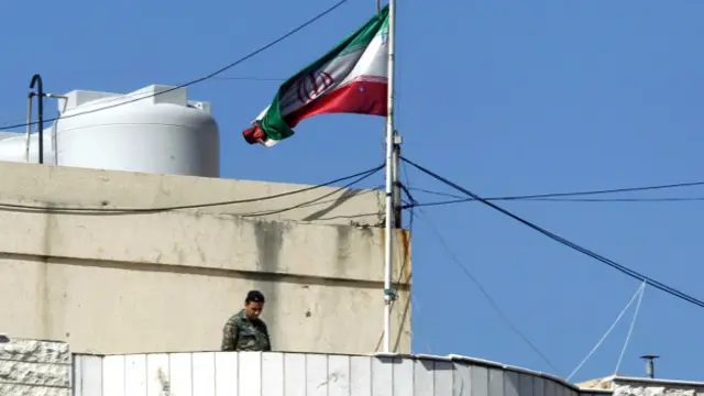 سرباز لبنانی زیر پرچم ایران که بخشی از آن پاره شده، نگهبانی میدهد