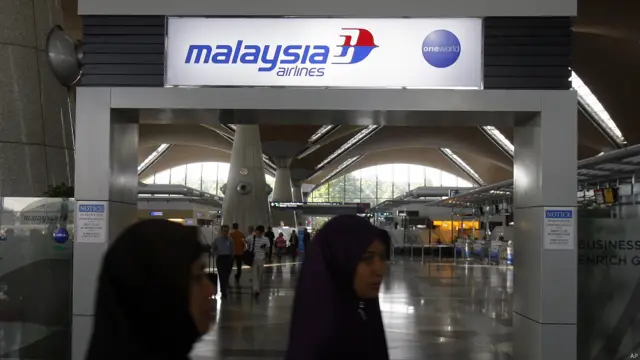 Các hành khách đi qua một biển hiệu của Hàng không Malaysia.