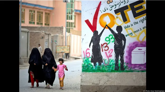 Mujeres y una niña pasan en la calle junto a una pancarta electoral Foto Anja Niedringhaus