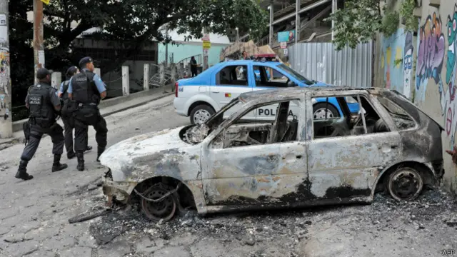 Policiais passam perto de carro incendiado na favela do Cantagalo (foto: AFP)