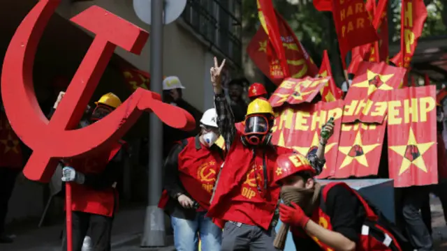 متظاهرون يلوحون بعلامة النصر، بينما يحتمي آخرون في اليوم العالمي للعمال.