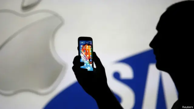 一名男子手持三星手站在在蘋果與三星產品廣告屏幕前(14/08/2013,資料照片)