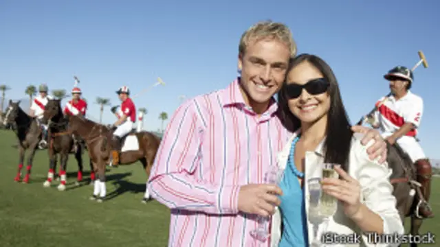 Pareja con copas de champán y un equipo de polo al fondo