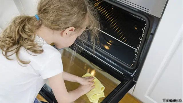 Una niña limpia un horno en casa