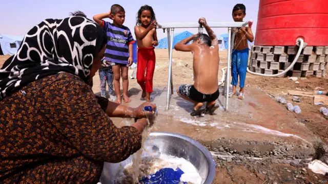 زن آواره عراقی لباس‌های کثیف اعضای خانواده را در اردوگاه موقت می‌شوید