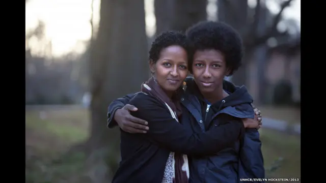 Nhiếp ảnh gia Evelyn Hockstein nói: "Người chú của Naima bị giết chết tại Ethiopia do tham gia phong trào Oromo. Cha mẹ của chị bỏ chạy khỏi Kenya như những người tỵ nạn chính trị, trước khi được cho tới California. Bây giờ, Naima [chụp chung cùng con trai trong hình này] làm nhân viên cho Ủy ban Cứu trợ Quốc tế ở Atlanta. "Tôi thích làm việc với khách hàng," chị nói. "Tôi nhìn thấy cha mẹ mình, thấy mình trong họ." Naima có kế hoạch tập trung vào sức khỏe phụ nữ và sức khỏe nói chung, để những người phụ nữ tỵ nạn có thể lên tiếng mạnh mẽ hơn.