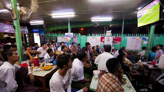 বার্মার রেংগুন শহরের ক্যাফে। বিশ্বকাপ উপলক্ষে চায়ের দোকানগুলো বড় পর্দায় খেলা দেখানোর ব্যবস্থা করেছে। গ্রুপ-বি'র এই ম্যাচে স্পেন অস্ট্রেলিয়াকে ৩-০ গোলে পরাজিত করে। (ছবি: বিবিসি বার্মিজ)