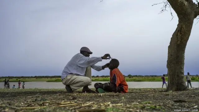 Un père coupe les cheveux de son fils à Melut sur les rives du Nil, Soudan du Sud