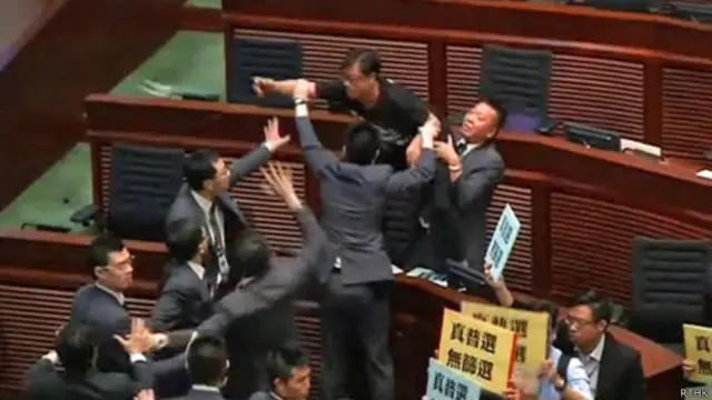 香港立法会议员黄毓民（上）向主席台方向抛掷物品（香港电台图片3/7/2014）