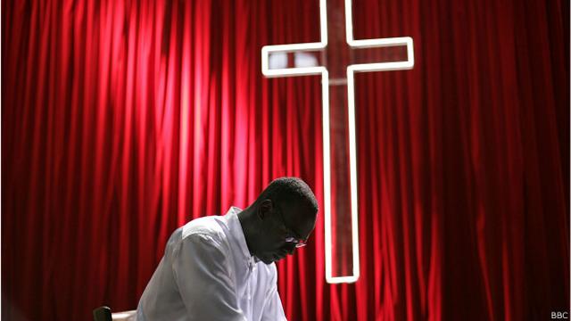 Священник молится на фоне креста