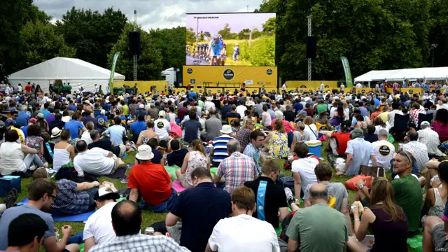 在伦敦海德公园，人们坐在草坪上，从大屏幕上观看比赛实况转播。
