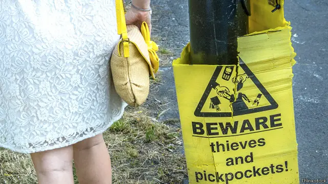 Девушка с сумочкой рядом с предупреждающей о карманниках табличкой