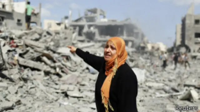 mulher aponta para prédio destruído