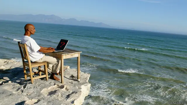 Hombre trabaja en su computadora, de frente al mar