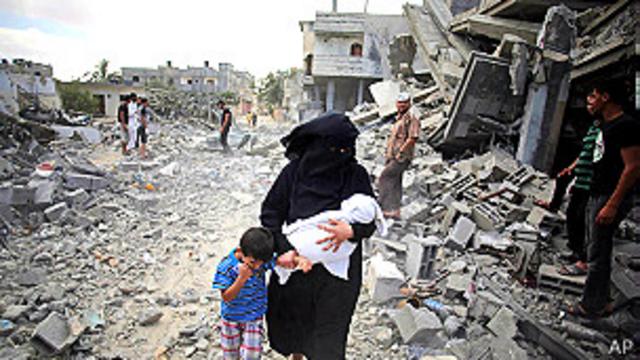 Una mujer camina con sus hijos en medio de escombros en Gaza