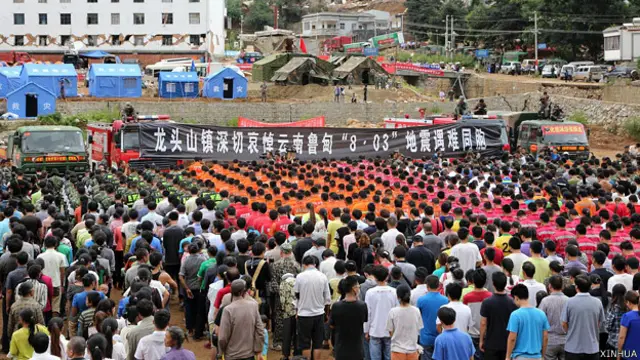 云南鲁甸龙头山镇灾民与救灾人员参与悼念地震死难者仪式（新华社图片10/8/2014）