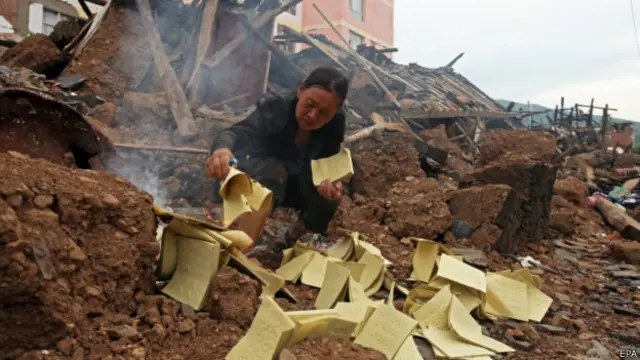 云南鲁甸龙头山镇一名灾民在已倒塌的房子旁焚烧纸钱悼念遇难家属（8/8/2014）