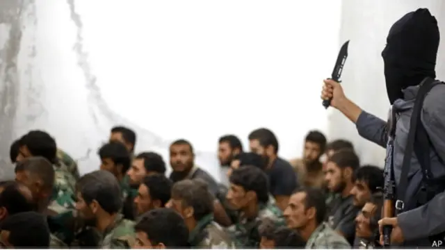 Seorang milisi DI memegang pisau dan tentara Suriah yang ditangkap di Taqba.