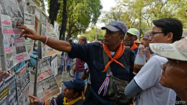 Pembaca melihat sejumlah berita utama dalam koran di Thailand.
