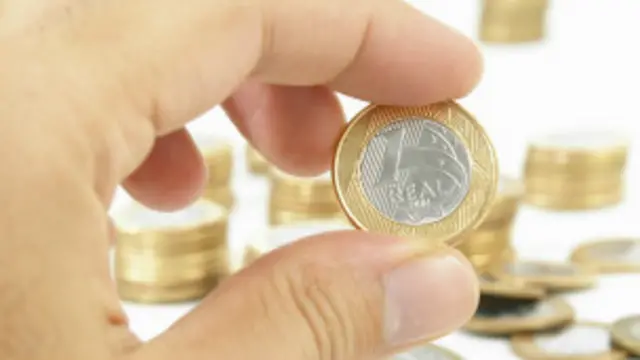 Una persona sostiene una moneda de un real entre sus dedos.