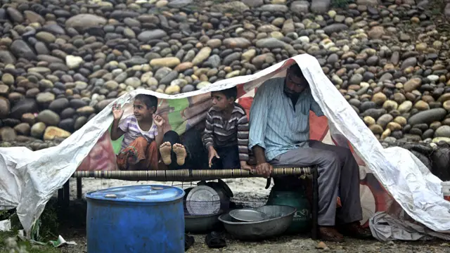 बरसात से बचने के लिए ख़ुद को प्लाटिक की एक चादर ओढ़े हुए एक परिवार. 