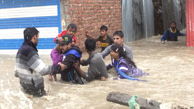 श्रीनगर में बाढ़ के पानी में घिरे हुए घरों से निकलकर सुरक्षित स्थानों की ओर जाते लोग.