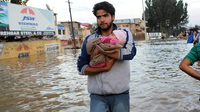 श्रीनगर में अपने नवजात बच्चे के साथ बाढ़ के पानी से गुजरता एक व्यक्ति