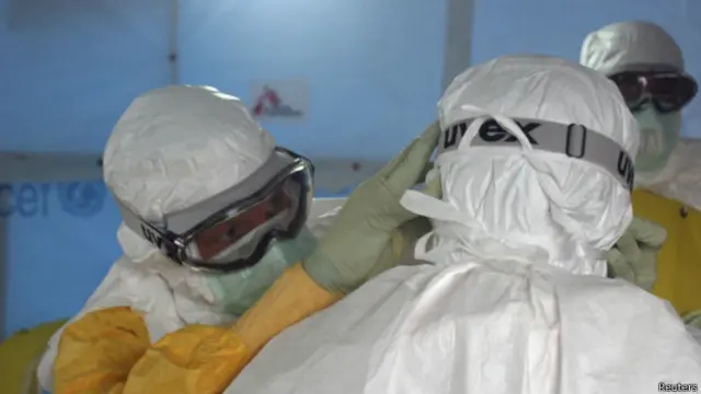 یکی از اعضای تیم پزشکی آمریکا در لیبریا به یک عضو دیگر تیم کمک می‌کند تجهیزاتش را محکم کند