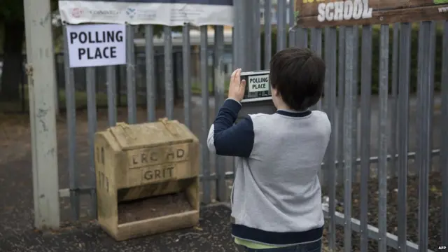 Um menino tira uma foto do lado de fora da seção eleitoral onde seus pais votaram na capital da Escócia, Edimburgo. 