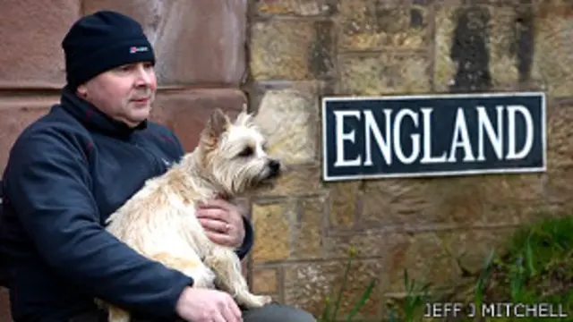 Hombre sentado junto a un cartel que dice "Inglaterra"