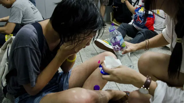 一名女子坐在地上，用瓶装水清洗脸面。