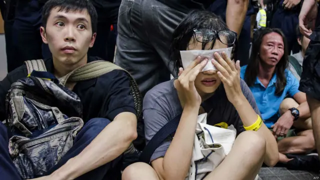 抗议者坐在地上，这名女子眼睛感到非常不适。
