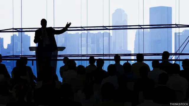 Un conferenciante le habla a una audiencia en la sombras