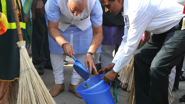 नई दिल्ली की वाल्मीकि बस्ती में झाड़ू लगाने के बाद कूड़ा उठाते प्रधानमंत्री नरेंद्र मोदी