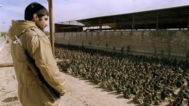 یک سرباز ایرانی در حال تماشای شماری از اسرای عراقی در کمپی در نزدیکی اهواز