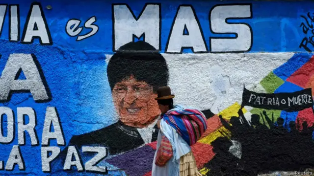 Una pintura de Evo Morales en una pared y una indígena que le pasa por enfrente