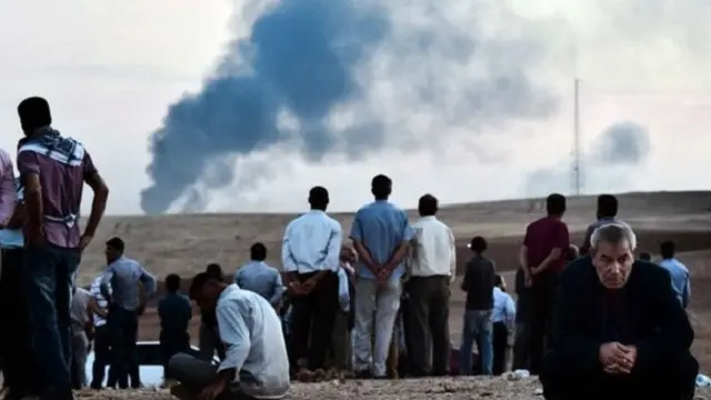 来自叙利亚边境科巴尼的库尔德难民远望激战中的家乡上空的黑烟。 