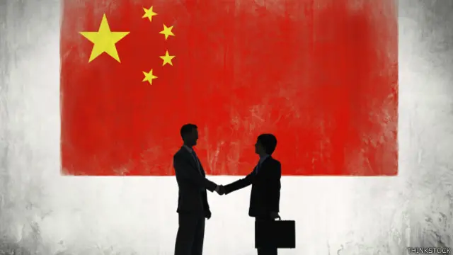 Dos ejecutivos se dan la mano. Al fondo, una bandera de China