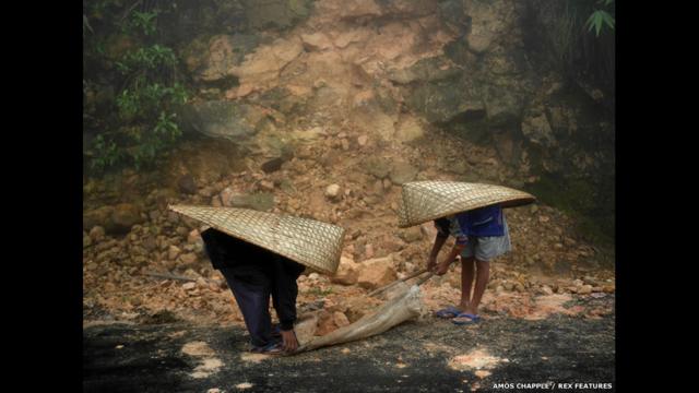 قرويون يرتدون مظلاتهم الخاصة أثناء العمل بالقرب من قرية ماوسينرام. عاوس تشابل/ ريكس فيتشرز