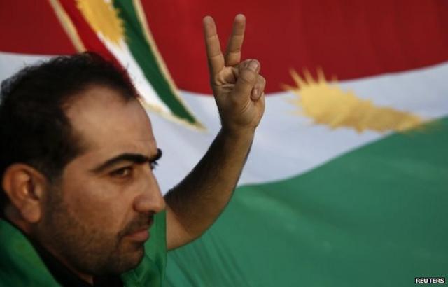 مواطن كردي يشير بعلامة النصر أمام العلم