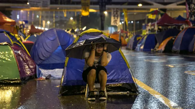 香港金钟夏悫道上一名“占领中环”年青示威者冒雨打伞留守于帐篷前（22/10/2014）