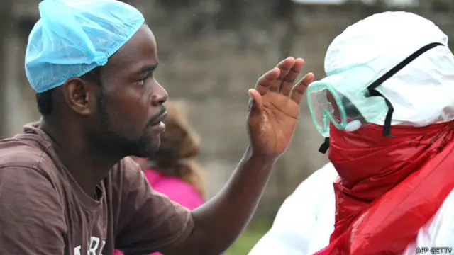 Dos hombres se ponen el traje protector en Liberia para recoger los restos de una víctima de la enfermedad